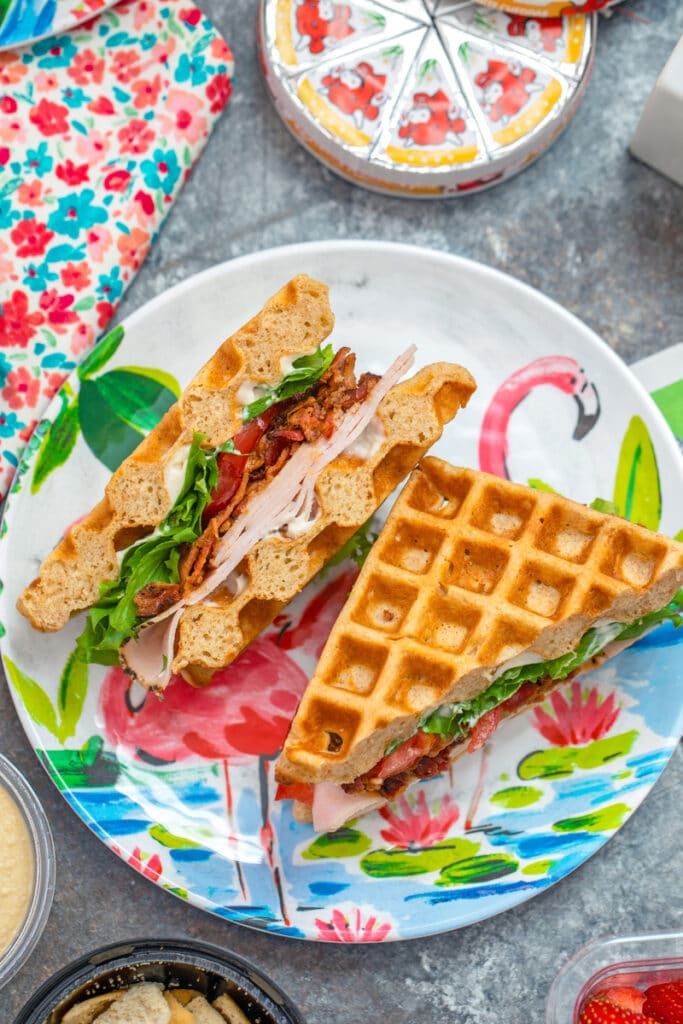 Overhead view of turkey BLT waffle sandwich on a fun flamingo plate with Laughing Cow cheese in background