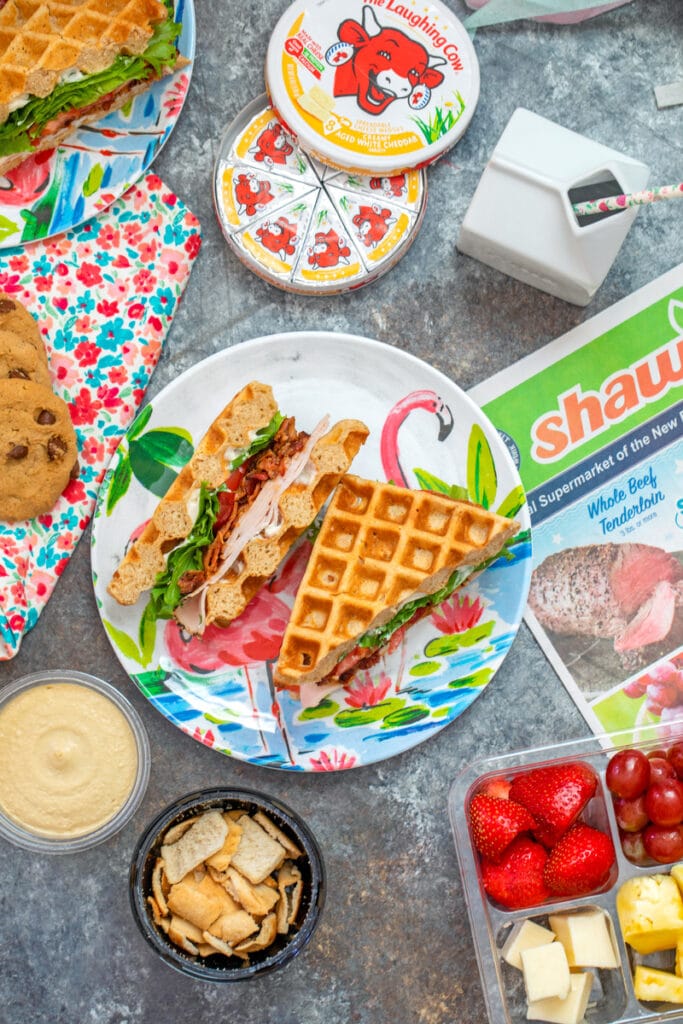 Overhead view of easy back-to-school lunch featuring turkey BLT waffle sandwich and all kinds of snacks