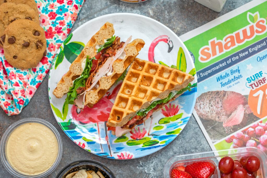 Overhead landscape view of a turkey BLT waffle sandwich surrounded by healthy back-to-school snacks