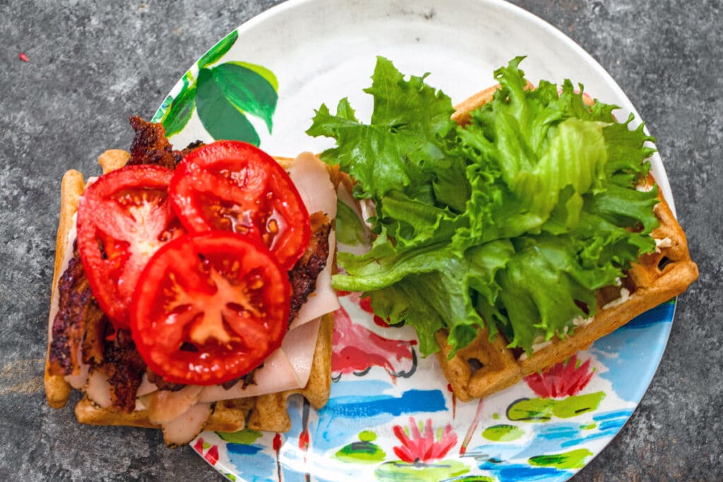 View of turkey BLT waffle sandwiches being made with bacon, tomatoes, deli turkey, and lettuce on waffles