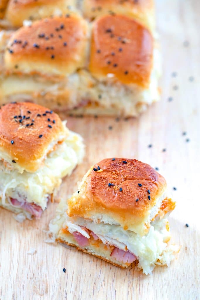 Overhead view of BBQ reuben sliders with one sandwich pulled away from the rest with golden tops and sauerkraut, turkey, ham, and cheese