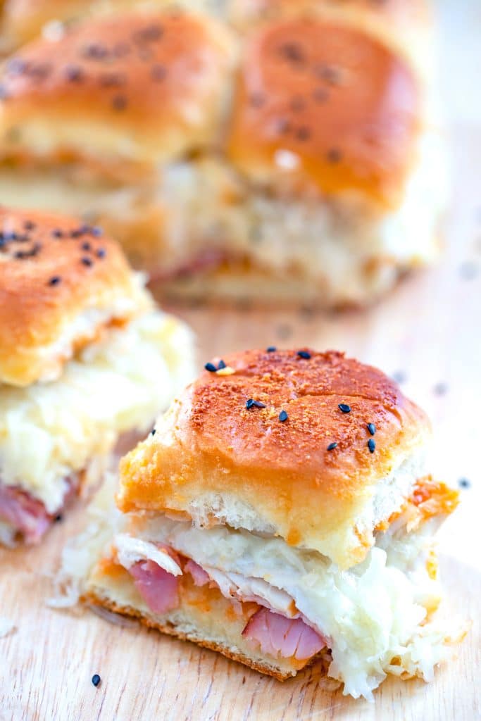 View of turkey, ham, and swiss BBQ reuben sliders sitting on a cutting board with one sandwich pulled away from the rest