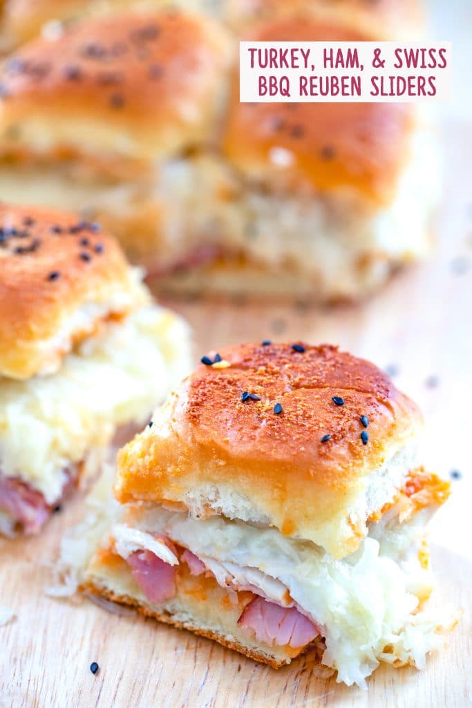 View of turkey, ham, and swiss BBQ reuben sliders sitting on a cutting board with one sandwich pulled away from the rest and recipe title labeled at top