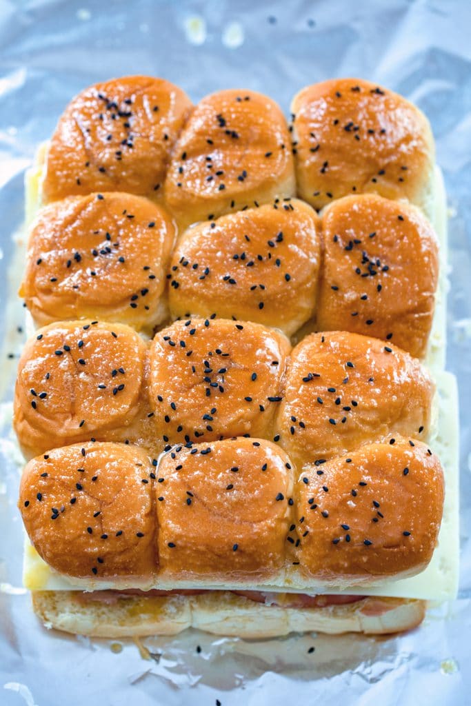 Overhead view of BBQ reuben sliders on a foil-lined baking dish and brushed with butter before they go in the oven