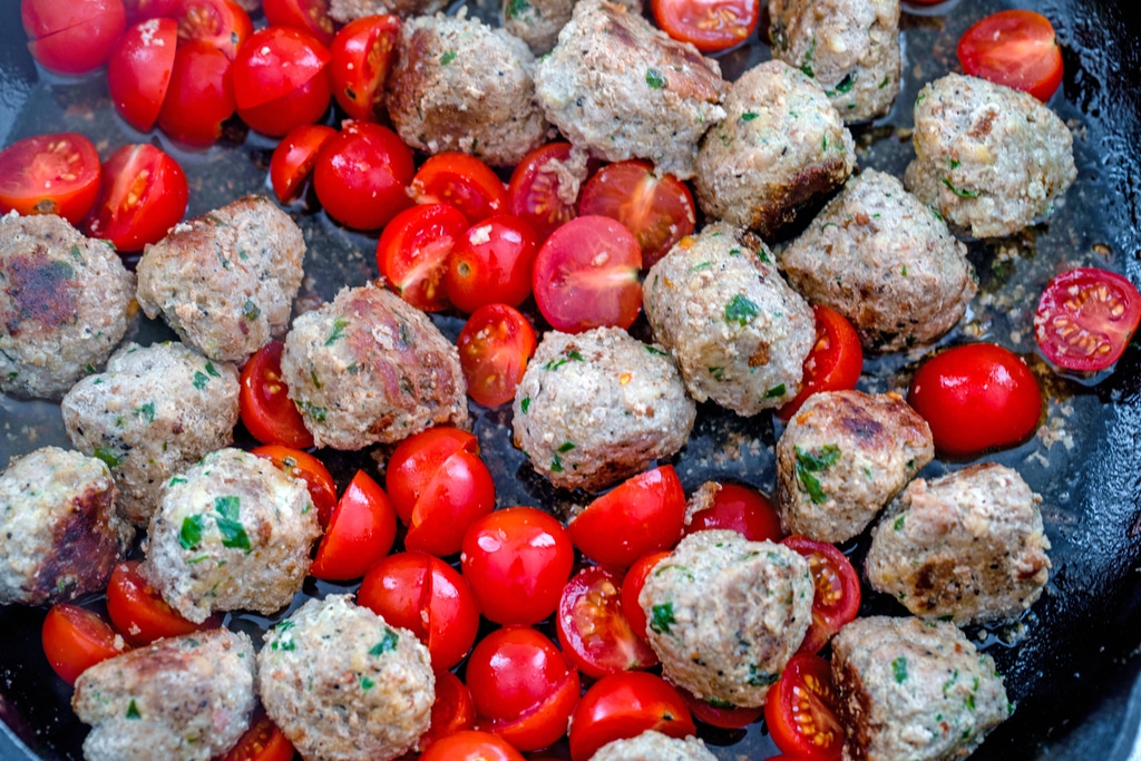 Turkey meatballs and halved tomatoes in a skillet with water