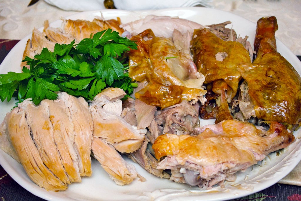 Platter with carved turkey on it, including sliced turkey breast, drumsticks, legs, and thighs with parsley garnish