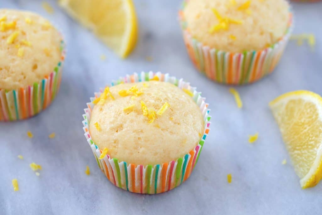 Landscape head-on photo of multiple Tuscan lemon muffins with lemon zest and lemon wedges scattered around