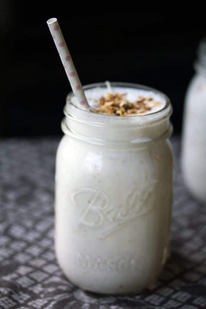 Head-on vide of vanilla coconut milkshake in a mason jar topped with toasted coconut and a pink polka dot straw with a black background