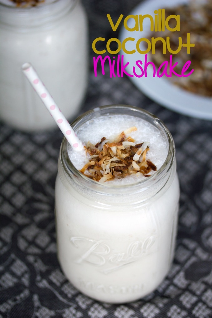 Close up of vanilla coconut milkshake in a mason jar topped with toasted coconut and a pink polka dot straw with a plate of toasted coconut in the background and "Vanilla Coconut Milkshake" text on top