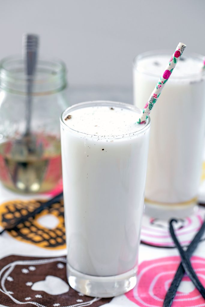 View of two vanilla egg creams with jar of vanilla simple syrup and vanilla beans in the background