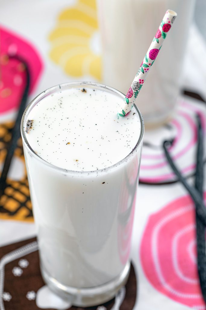 Overhead closeup view of a vanilla egg cream with a flower straw with vanilla beans in the background