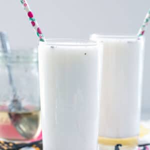 Head-on view of a glass of vanilla egg cream with second glass in background and vanilla beans all around.