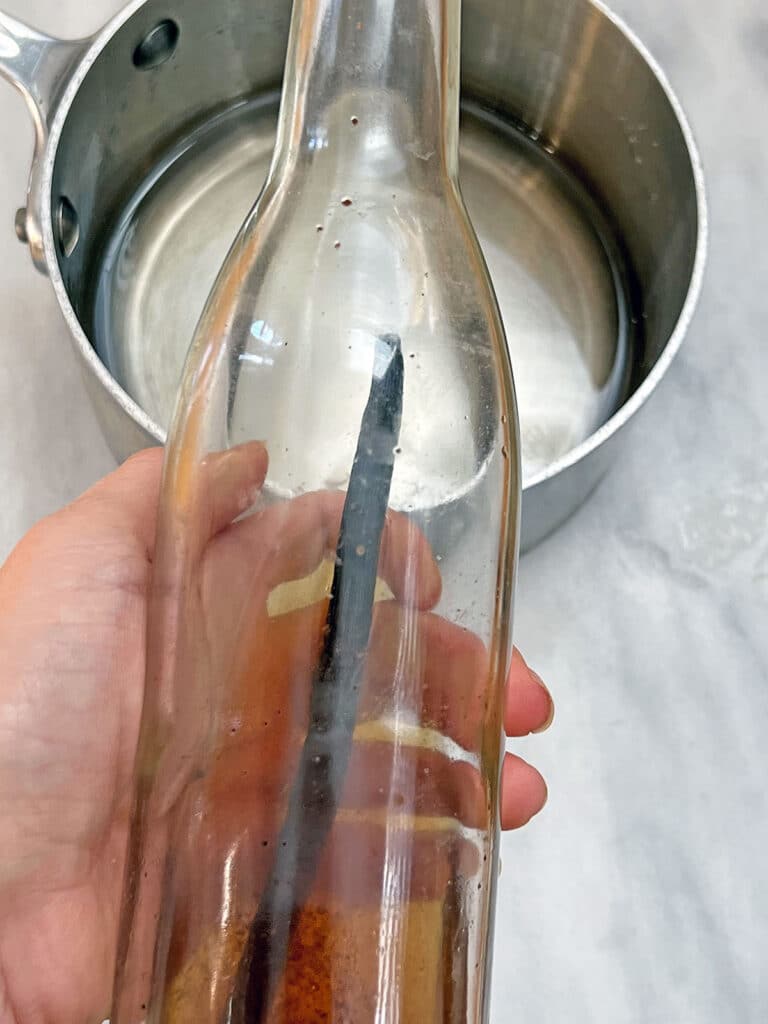 Vanilla extract bottle held over simple syrup in saucepan.