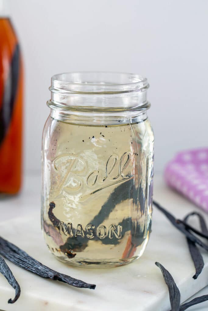 Head-on closeup view of mason jar of vanilla syrup in mason jar with vanilla beans all around.