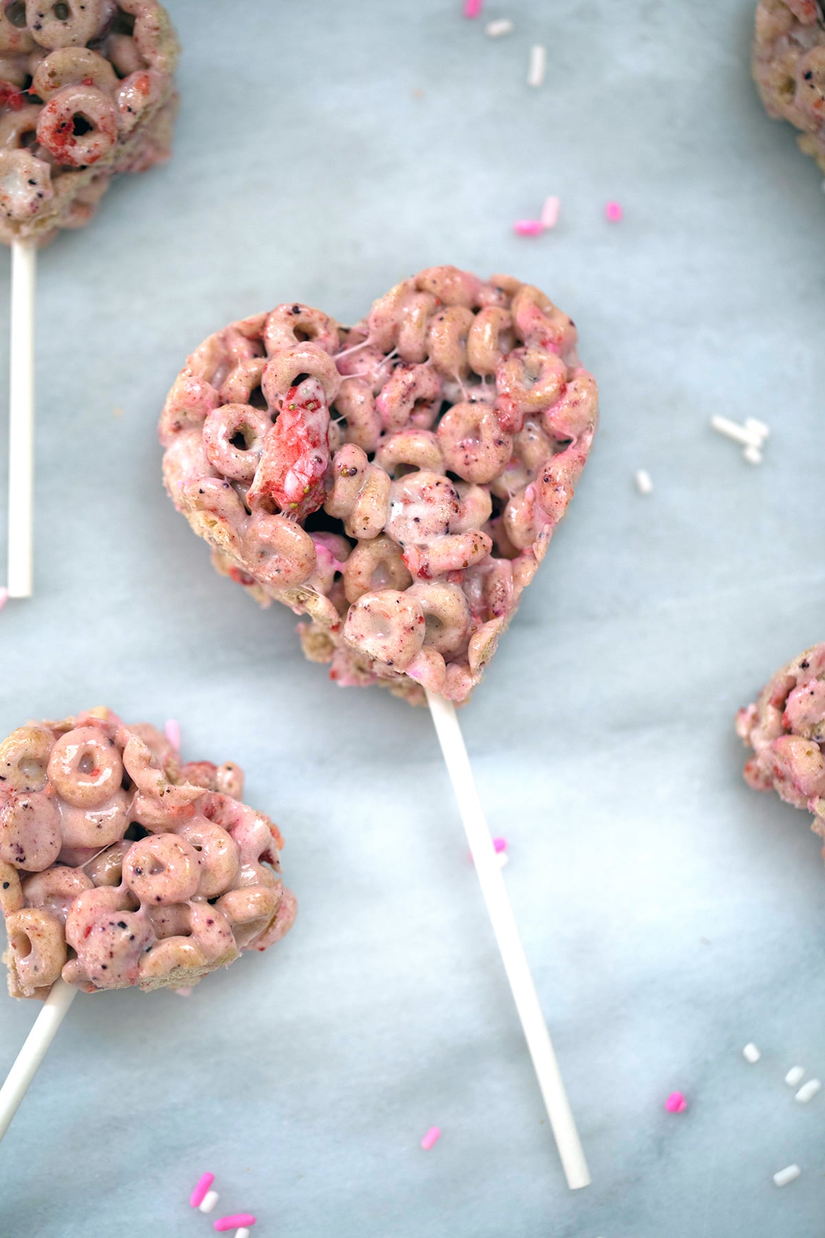 Overhead view of pink heart-shaped Very Berry Cheerios Treats on a popsicle stick on a marble surface.