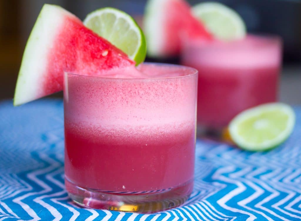 Landscape view of a watermelon coconut cocktail with watermelon wedge and lime round garnish with second cocktail in the background