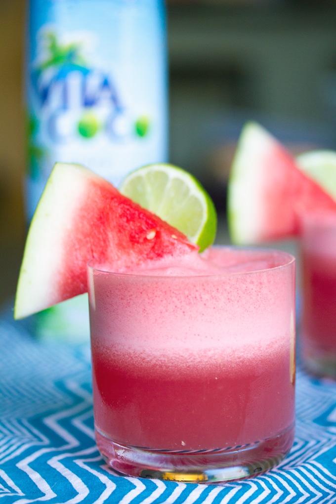 Head-on view of watermelon coconut cocktail with watermelon wedge and lime garnish and carton of coconut water in the background