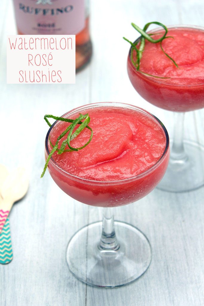 Overhead view of two glasses of watermelon rosé slushies with lime zest garnish, two wooden spoons, and bottle of rosé in the background with recipe title at top