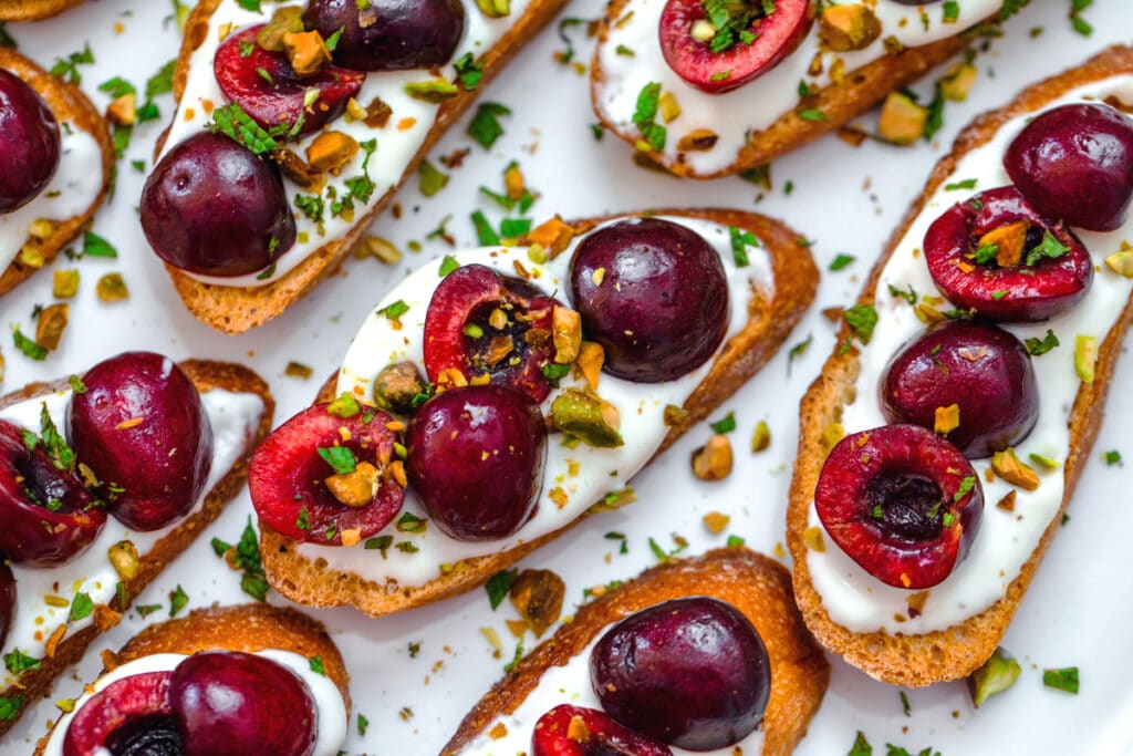 Landscape closeup of whipped ricotta cherry crostini with pistachios and mint
