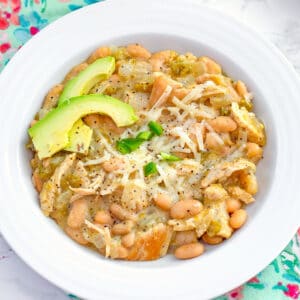 Overhead closeup view of a bowl of white chicken chili topped with cheese, avocado, and jalapeño.