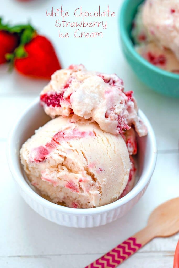 Overhead view of white bowl of white chocolate strawberry ice cream with strawberries, pink wooden spoon, and second bowl in the background and "White Chocolate Strawberry Ice Cream" text at top