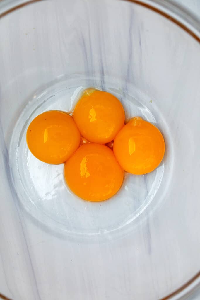 Four golden yellow egg yolks in bowl