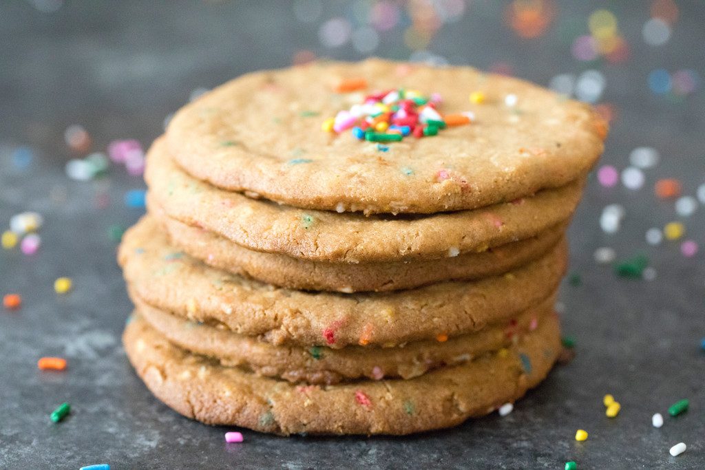 Landscape view of a stack of XL peanut butter cookies on a dark surface surrounded by sprinkles