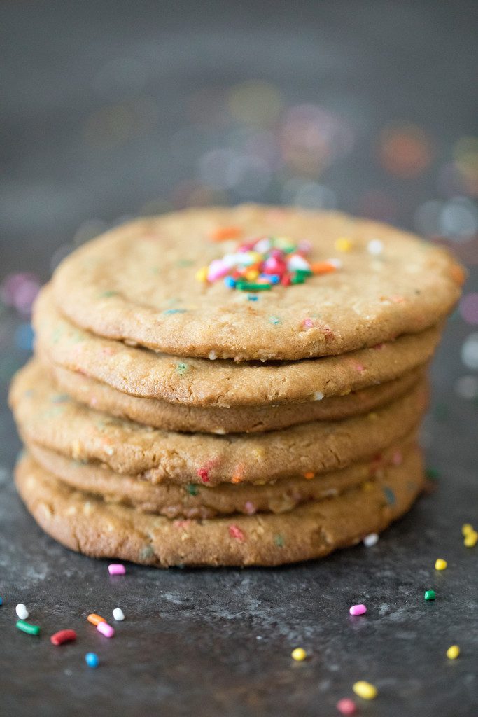 Head-on view of a stack of XL peanut butter cookies with sprinkles on a dark surface surrounded by sprinkles