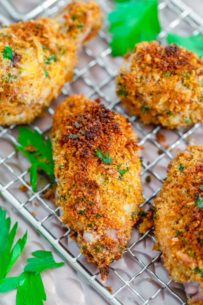 Overhead view of multiple zesty baked chicken wings on a baking rack with chopped parsley all around.