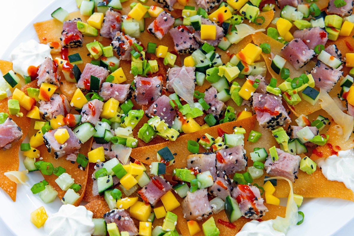 Landscape closeup view of ahi tuna nachos on wonton chips with cucumber, mango, avocado, and cilantro.