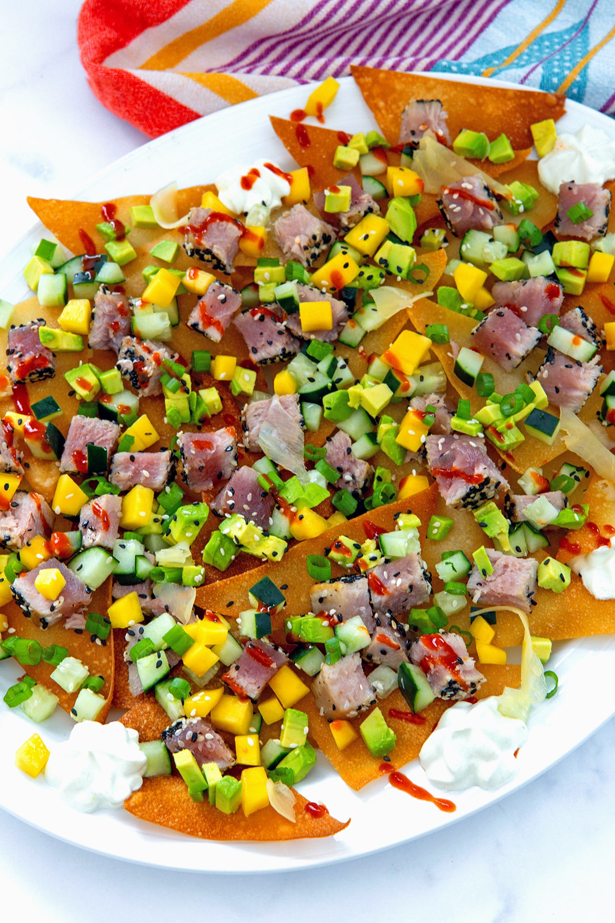 Overhead view of a platter of ahi tuna nachos on wonton chips with mango, cucumber, and avocado.
