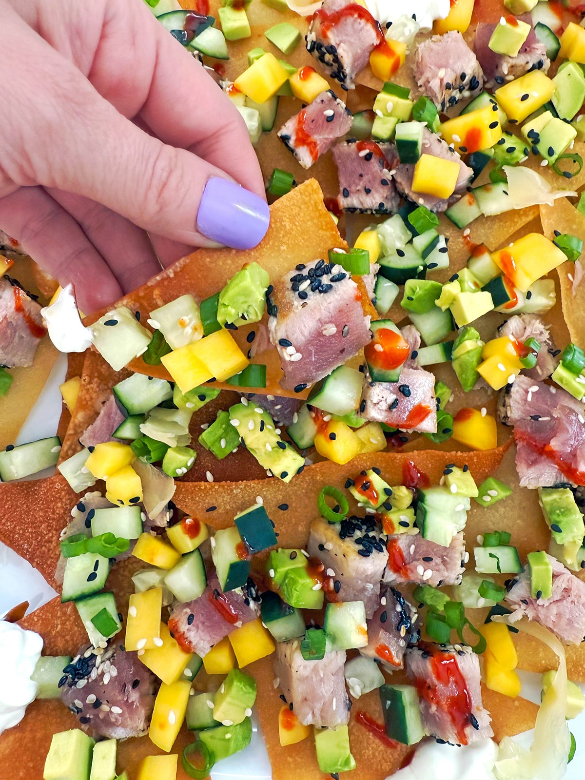 Hand holding an ahi tuna nacho with lots of toppings.