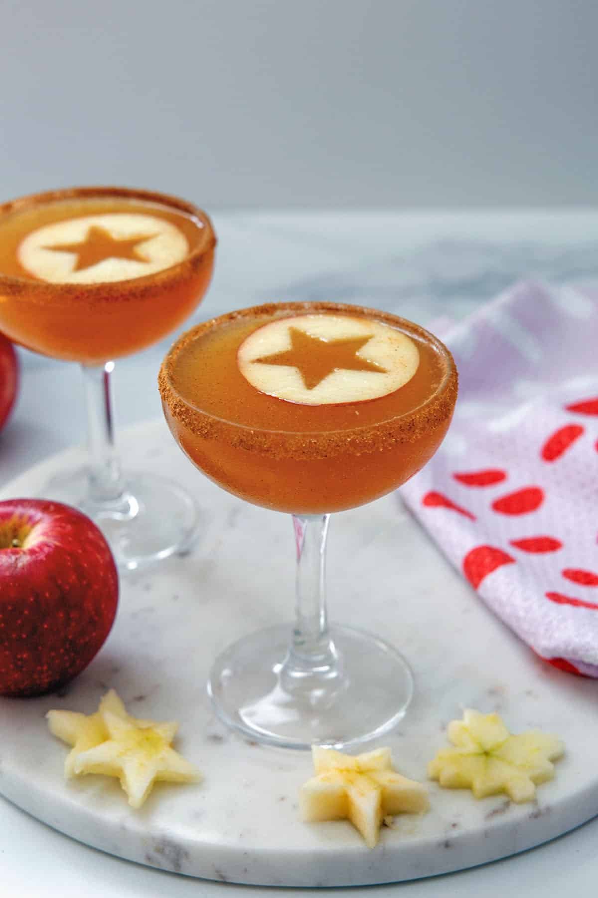 Two apple cider martinis in coup glasses with stars cut out of apple rounds.