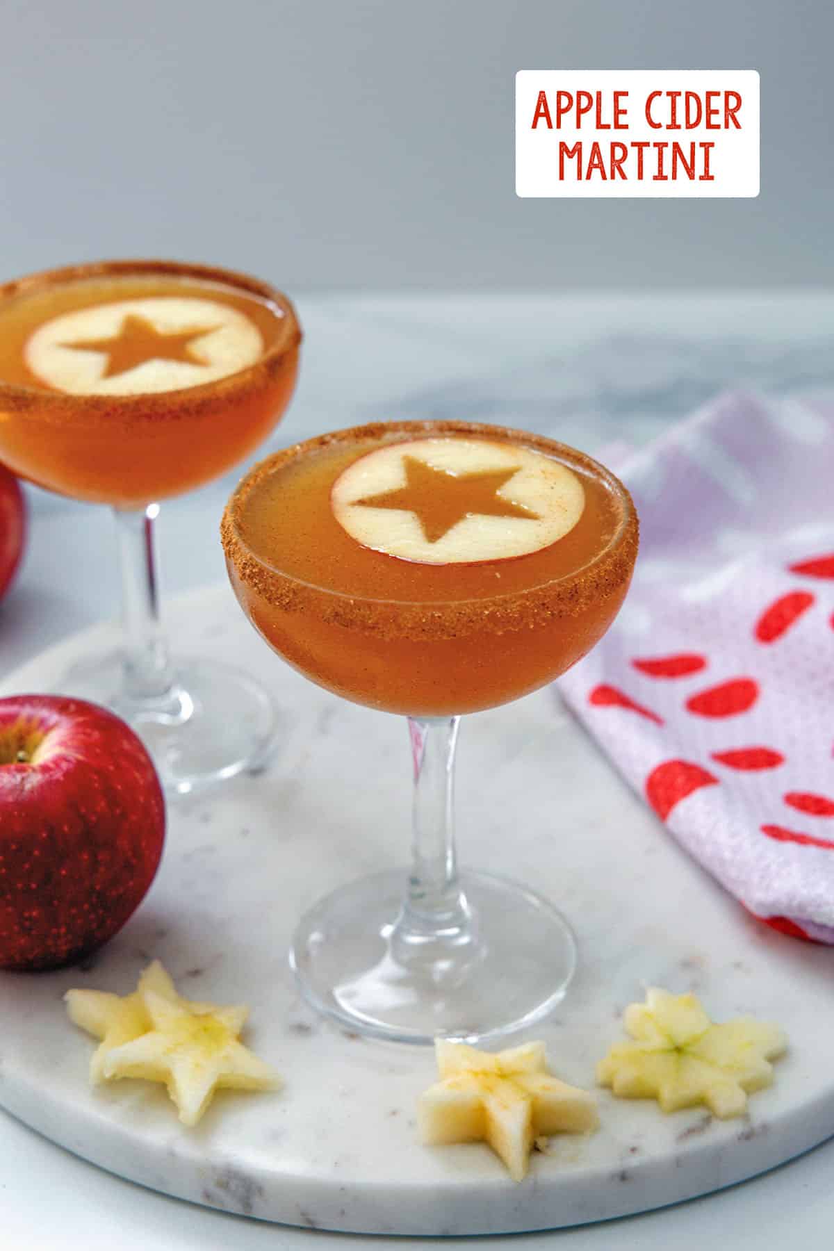 Two apple cider martinis in coup glasses with stars cut out of apple rounds with recipe title at top.