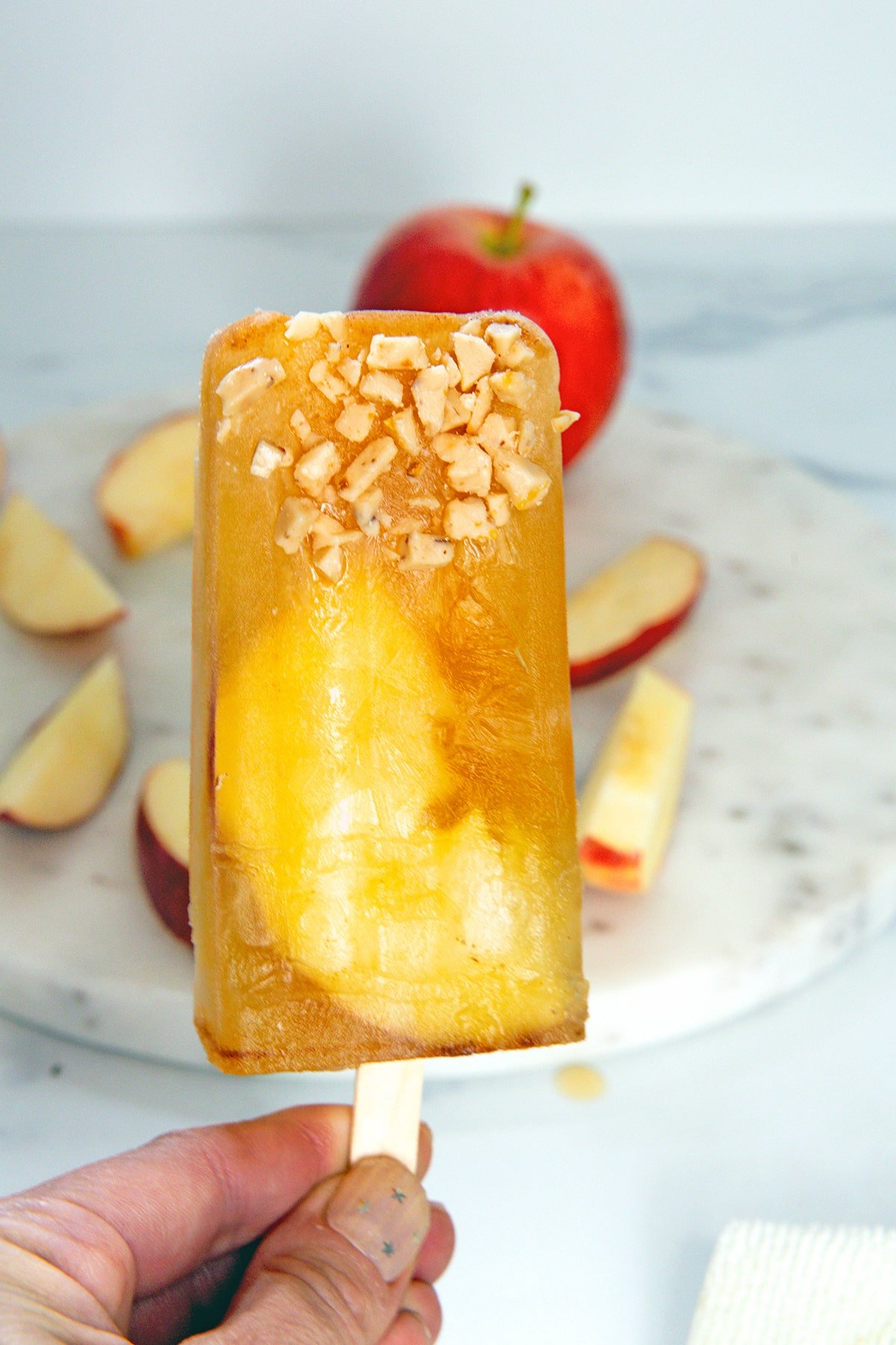 Hand holding an apple cider popsicle with toffee bits.