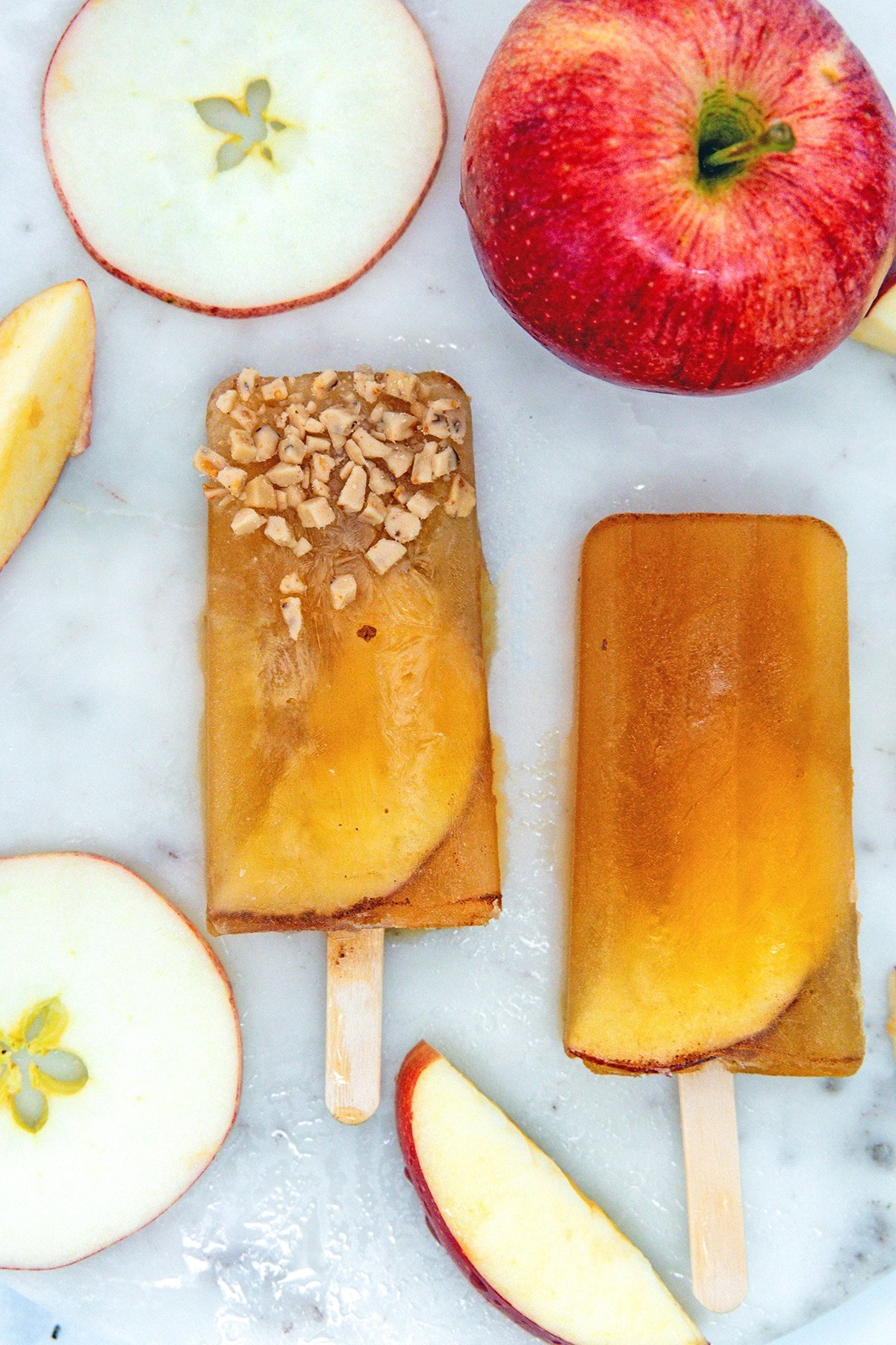 Overhead view of apple cider popsicles on a marble surface with apple slices.