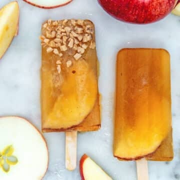 Closeup view of two apple cider popsicles on marble surface with apple slices.