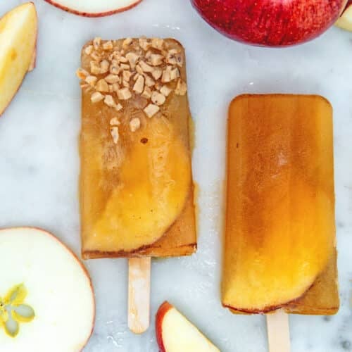 Closeup view of two apple cider popsicles on marble surface with apple slices.