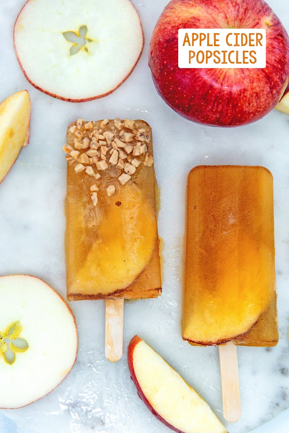 Overhead view of apple cider popsicles on a marble surface with apple slices and recipe title at top.