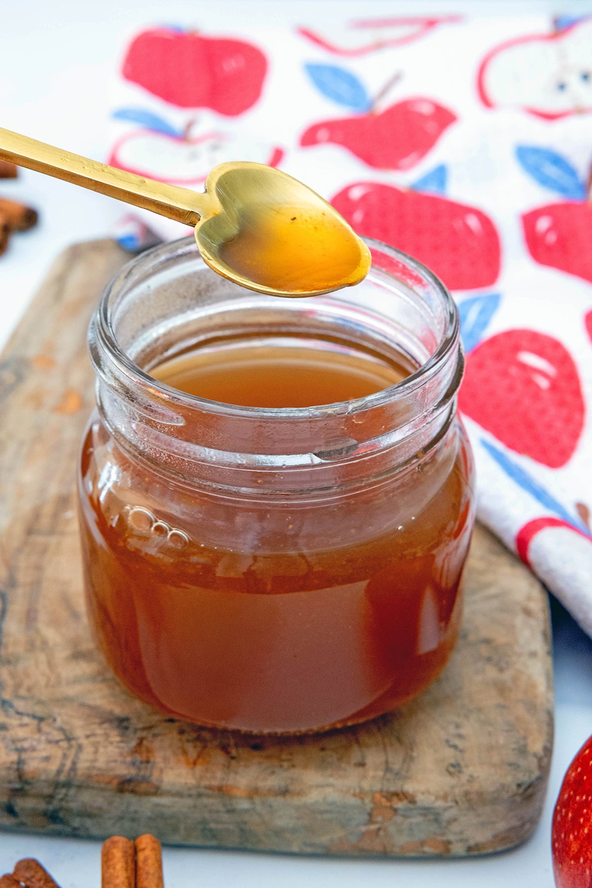 Overhead view of a jar of apple cider syrup with spoon being held over it.