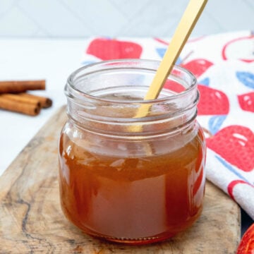 Closeup view of a jar of apple cider syrup with gold spoon.