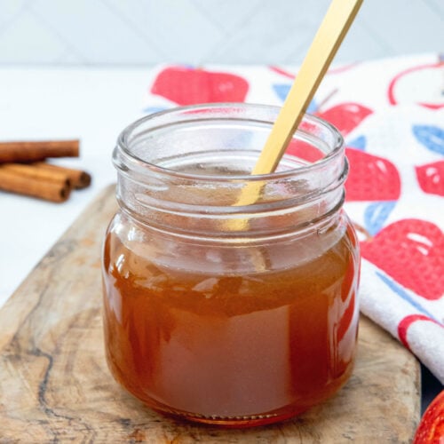 Closeup view of a jar of apple cider syrup with gold spoon.