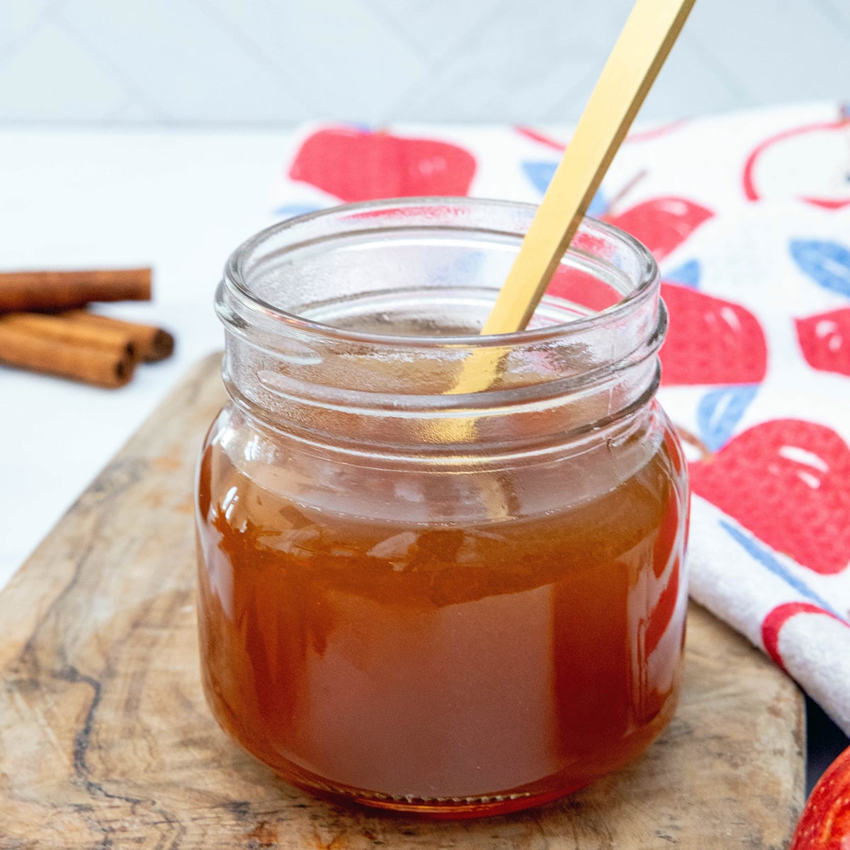 Closeup view of a jar of apple cider syrup with gold spoon.