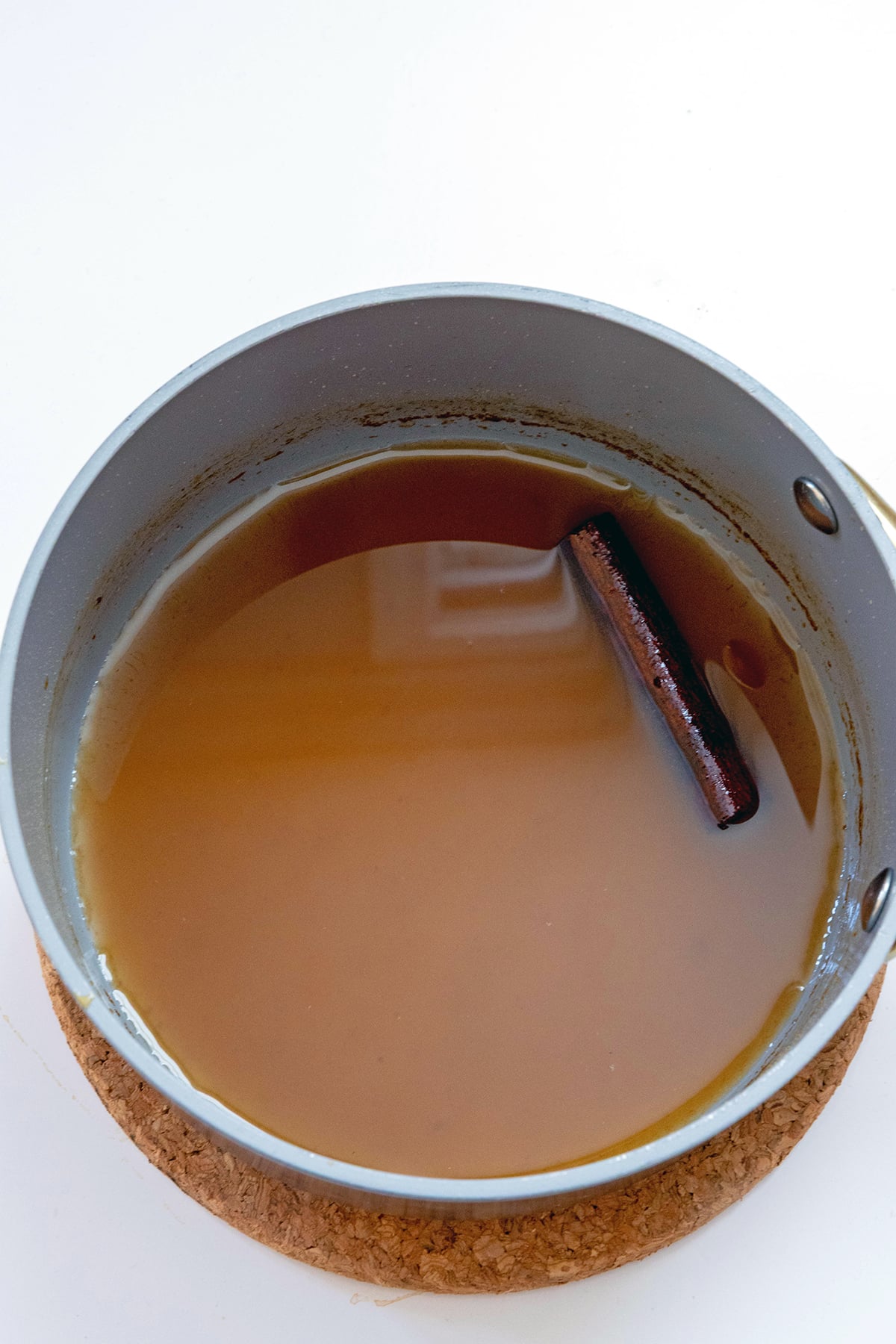 Overhead view of apple cider syrup in a saucepan with cinnamon stick.