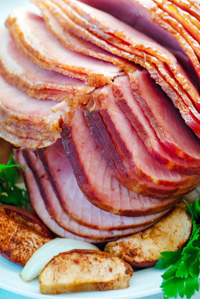 Close-up of spiral cut slices of apple spice glazed ham with apples and onions around