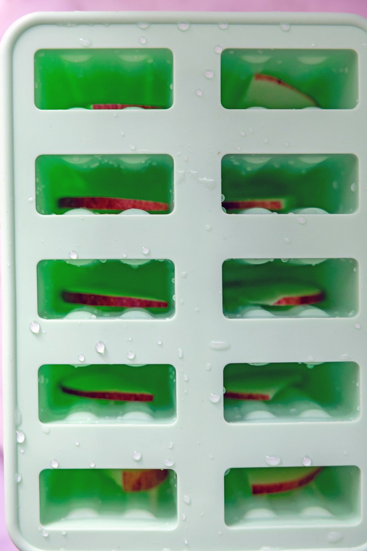 Overhead view of popsicle molds with apple slices in them.