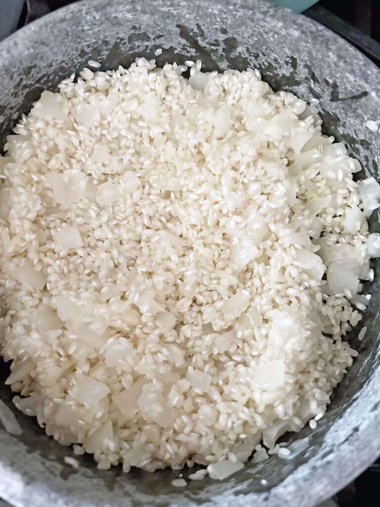 Arborio rice with onions and garlic in pot.