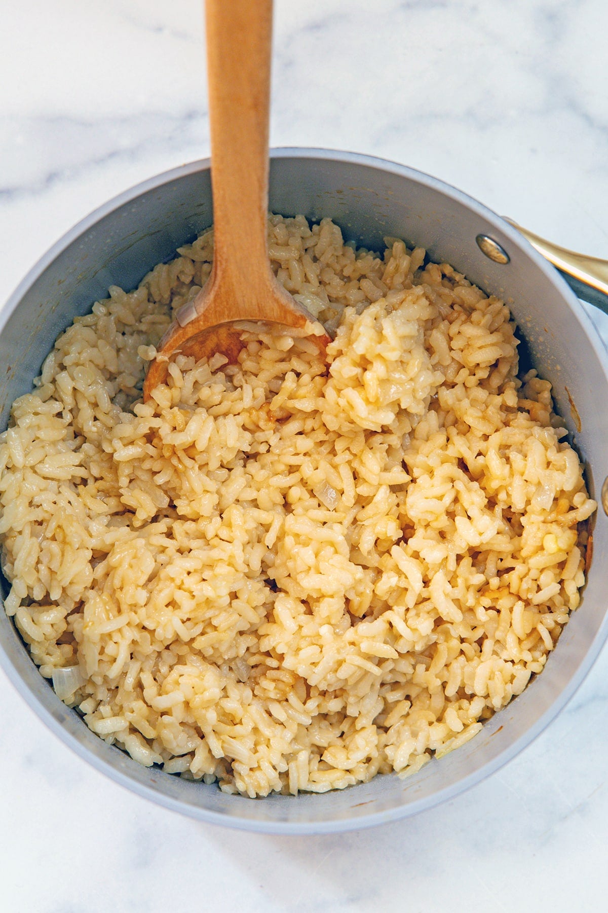 Overhead view of arborio rice in saucepan with chicken broth and wooden spoon.