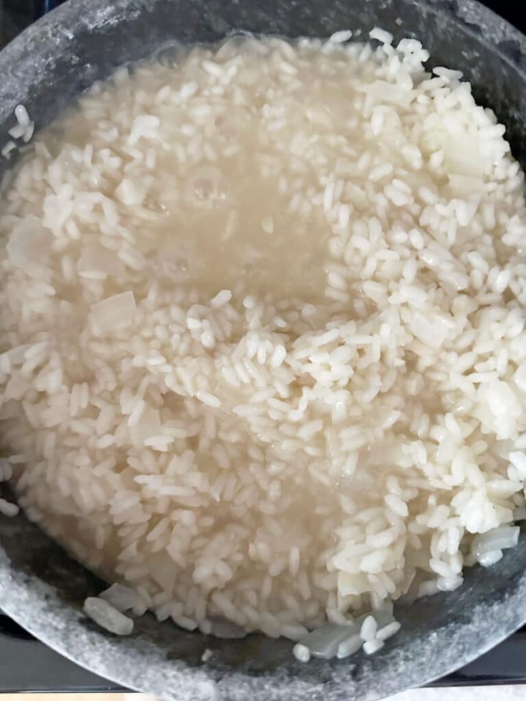 Chicken broth added to arborio rice in pot.