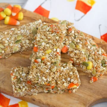 Closeup view of candy corn granola bars on a wooden board with candy corns in background.